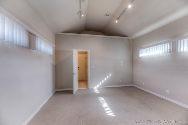 spare room with visible vents, track lighting, baseboards, vaulted ceiling, and carpet floors