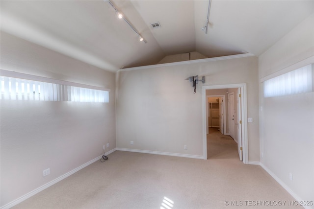 spare room with lofted ceiling, rail lighting, light colored carpet, and visible vents