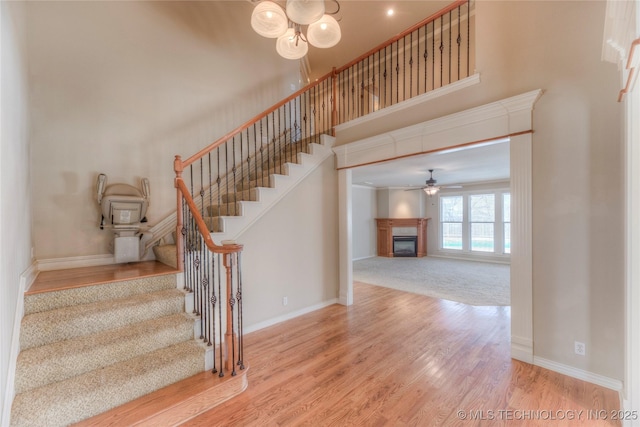 stairs featuring wood finished floors, baseboards, a ceiling fan, a towering ceiling, and a glass covered fireplace