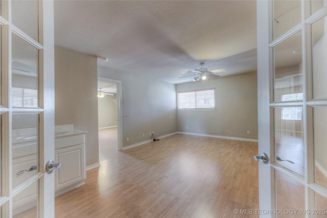 unfurnished room featuring ceiling fan, a textured ceiling, baseboards, and light wood-style floors