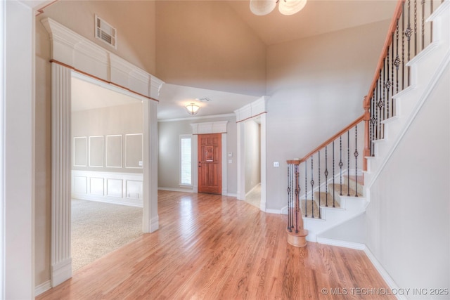 entrance foyer featuring visible vents, light wood-style floors, a towering ceiling, and stairs