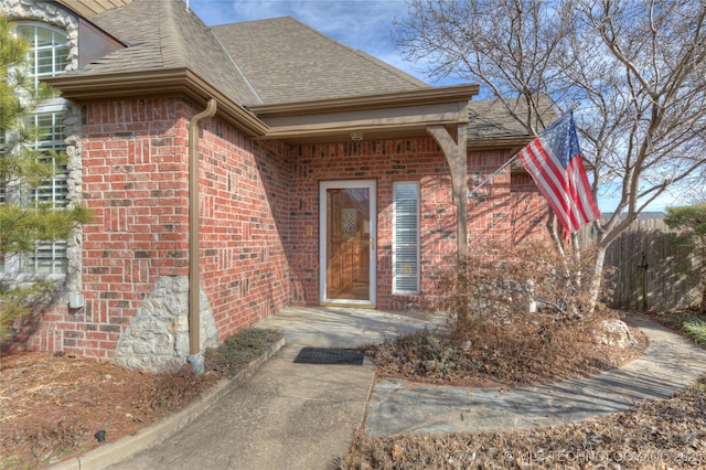 doorway to property featuring brick siding and roof with shingles