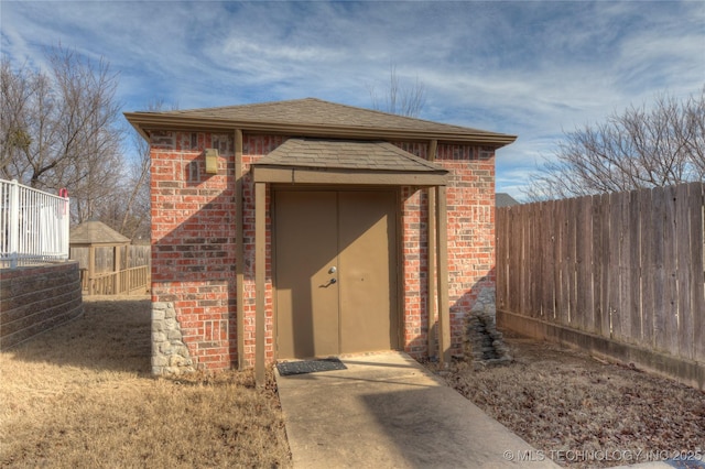 property entrance featuring fence, brick siding, and roof with shingles