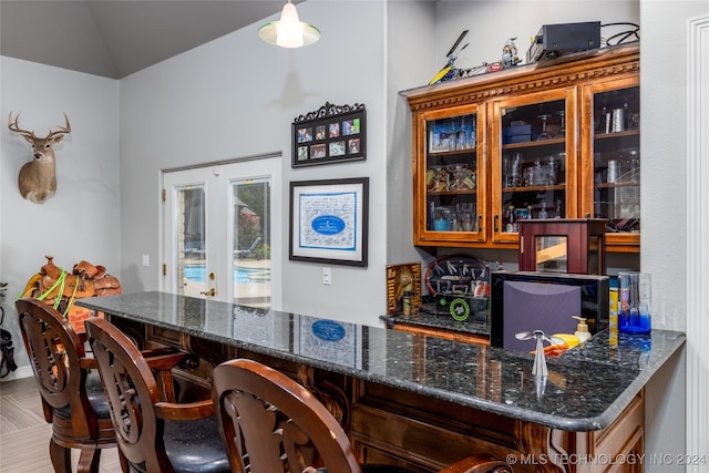 bar featuring dark stone countertops, vaulted ceiling, and pendant lighting