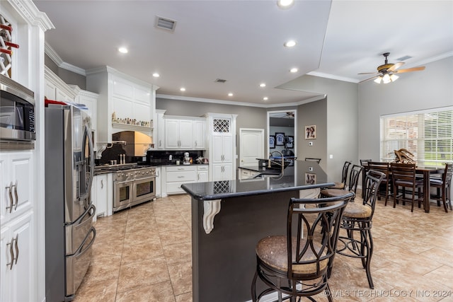 kitchen with stainless steel appliances, white cabinetry, ceiling fan, a kitchen island with sink, and a breakfast bar