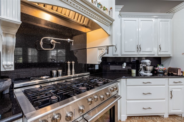 kitchen featuring dark stone countertops, backsplash, white cabinets, and high end range