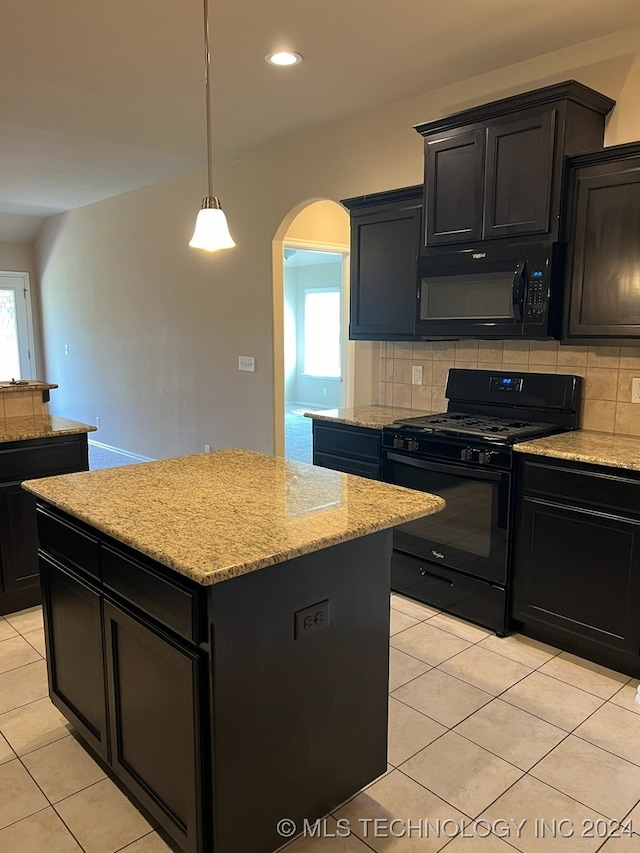 kitchen with decorative light fixtures, black appliances, a center island, decorative backsplash, and light stone counters