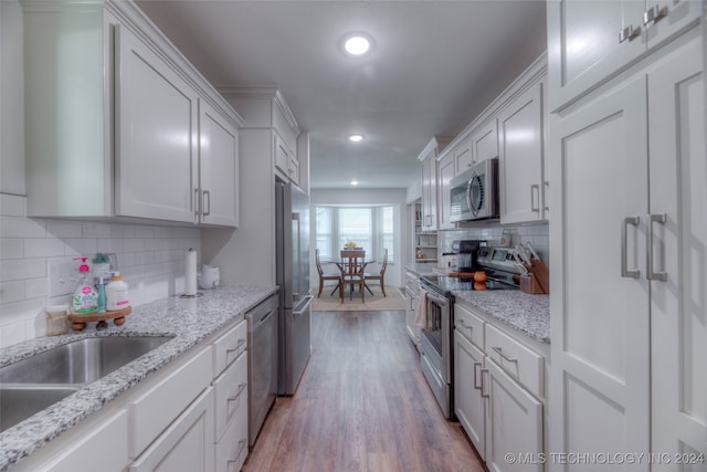 kitchen with backsplash, light hardwood / wood-style floors, stainless steel appliances, white cabinetry, and light stone counters