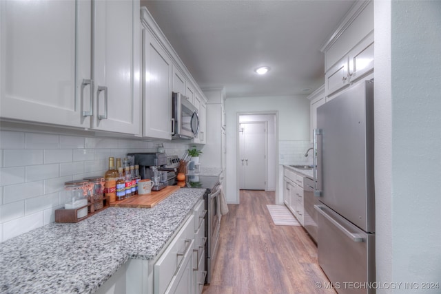 kitchen with light wood-type flooring, light stone countertops, stainless steel appliances, white cabinetry, and decorative backsplash