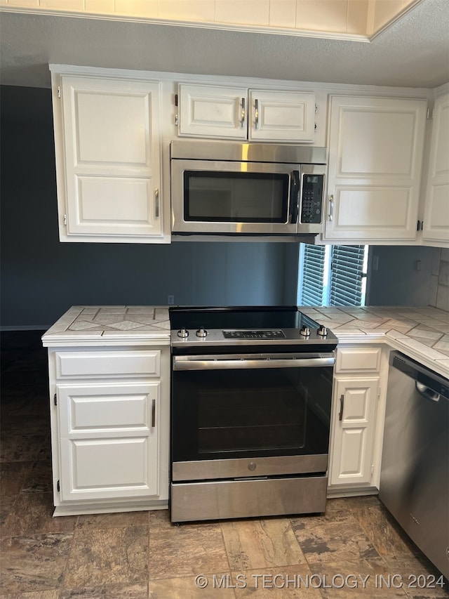 kitchen with appliances with stainless steel finishes, white cabinetry, tile counters, and a textured ceiling