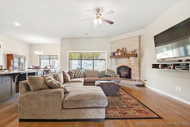 living room featuring ceiling fan with notable chandelier, light hardwood / wood-style flooring, and a brick fireplace