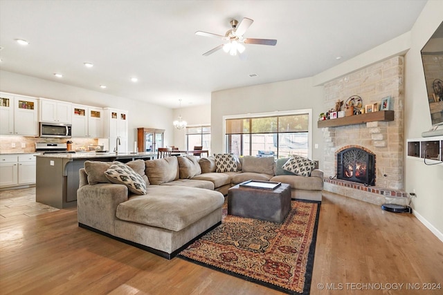 living room featuring light wood-type flooring, ceiling fan with notable chandelier, a stone fireplace, and sink