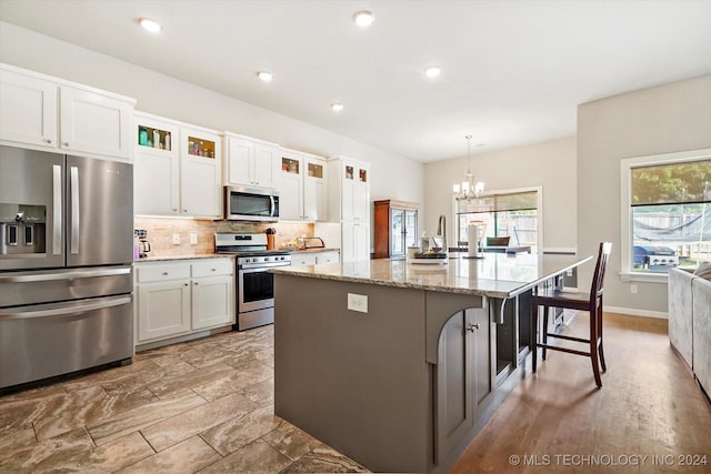 kitchen featuring white cabinetry, stainless steel appliances, decorative light fixtures, a kitchen bar, and a center island with sink