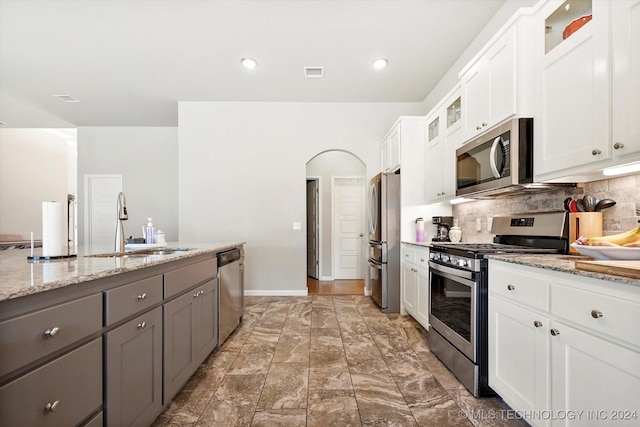 kitchen with backsplash, light stone counters, stainless steel appliances, sink, and white cabinetry