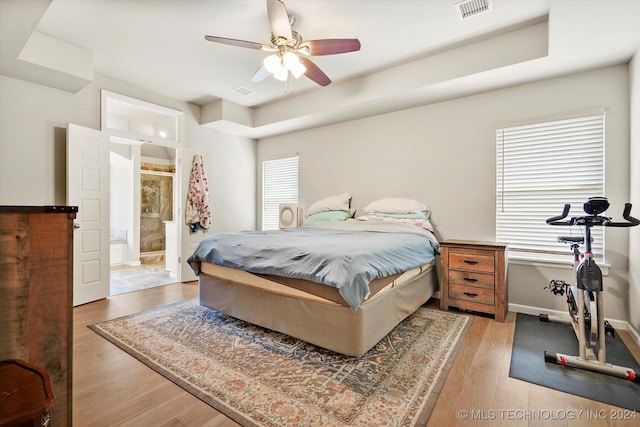 bedroom featuring ceiling fan, wood-type flooring, a tray ceiling, and ensuite bath