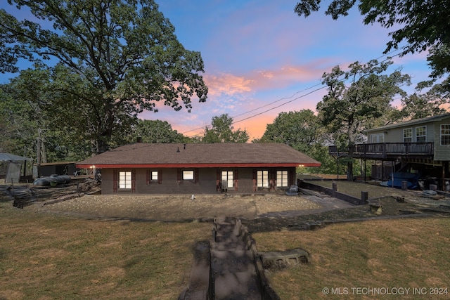 back house at dusk with a lawn and a deck