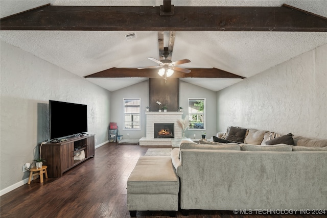 living room with a textured ceiling, dark wood-type flooring, a brick fireplace, and vaulted ceiling with beams