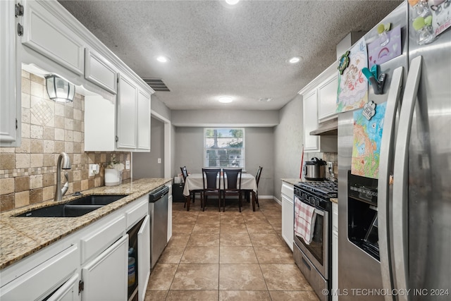 kitchen featuring light stone countertops, light tile patterned floors, appliances with stainless steel finishes, sink, and white cabinetry