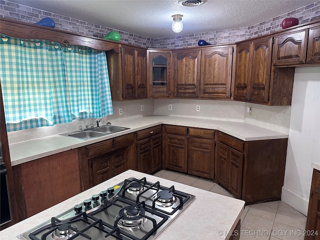 kitchen with stainless steel gas cooktop, a textured ceiling, light tile patterned floors, sink, and dark brown cabinetry