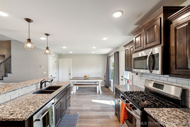 kitchen with appliances with stainless steel finishes, light wood-type flooring, dark brown cabinets, decorative light fixtures, and sink