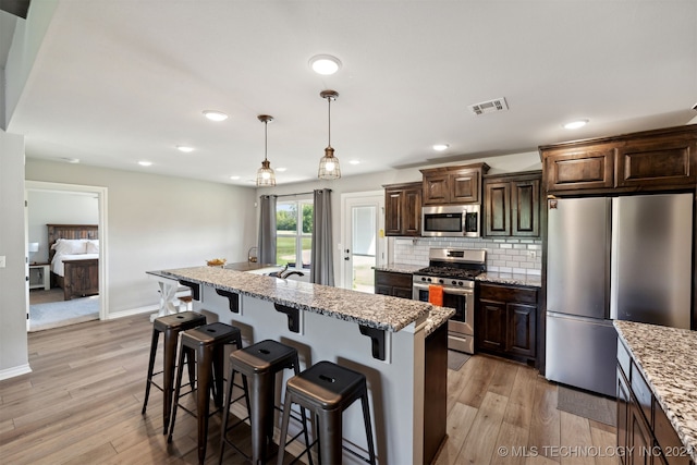 kitchen with dark brown cabinetry, a center island with sink, stainless steel appliances, and light hardwood / wood-style flooring