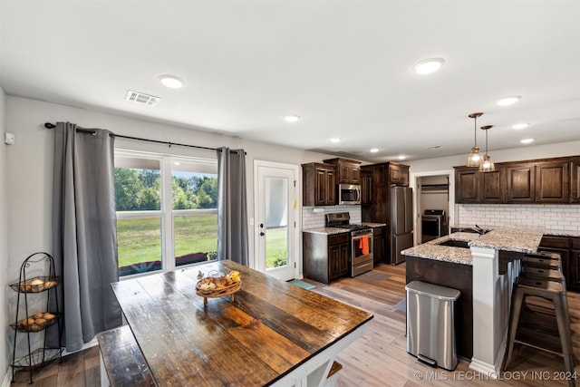 kitchen with stainless steel appliances, light stone counters, light wood-type flooring, and backsplash