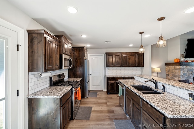 kitchen featuring dark brown cabinetry, hanging light fixtures, sink, stainless steel appliances, and light hardwood / wood-style floors