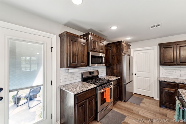 kitchen featuring appliances with stainless steel finishes, dark brown cabinets, light wood-type flooring, and light stone countertops