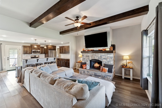 living room featuring light wood-type flooring, a stone fireplace, ceiling fan, and beamed ceiling