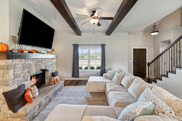 living room with a stone fireplace, beamed ceiling, ceiling fan, and hardwood / wood-style flooring