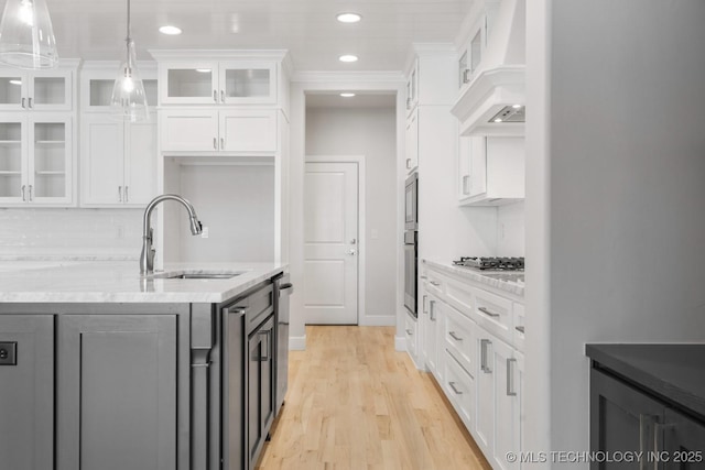 kitchen with custom range hood, appliances with stainless steel finishes, glass insert cabinets, white cabinetry, and a sink