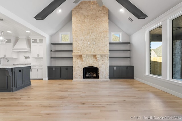 unfurnished living room with light wood finished floors, baseboards, visible vents, a fireplace, and high vaulted ceiling