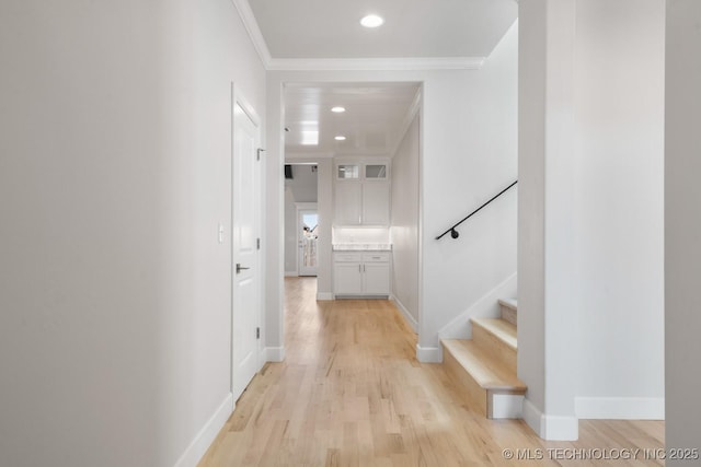 hallway with light wood-style floors, baseboards, and crown molding