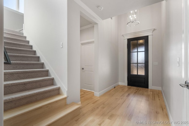 foyer featuring light wood-type flooring, a notable chandelier, stairway, and baseboards