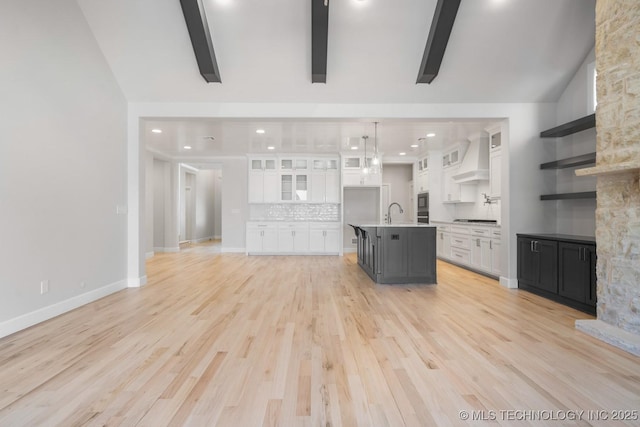 unfurnished living room with vaulted ceiling with beams, light wood-style flooring, baseboards, and a sink