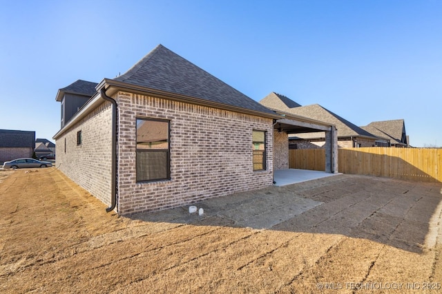 view of front of house with a patio, brick siding, a shingled roof, and fence