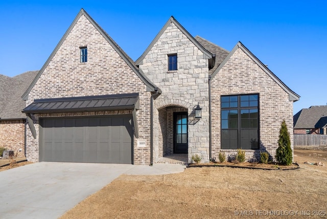 french country home with a garage, driveway, brick siding, and stone siding