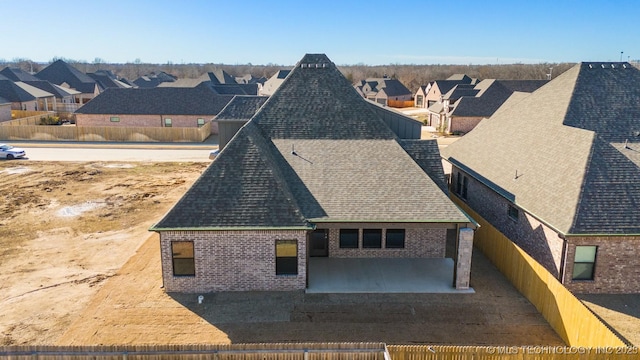 view of front of home with brick siding, roof with shingles, a patio area, and a residential view