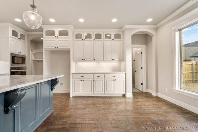 kitchen with pendant lighting, white cabinets, light stone countertops, built in microwave, and black oven