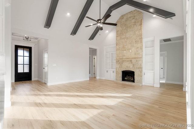 unfurnished living room featuring built in shelves, ceiling fan with notable chandelier, beam ceiling, high vaulted ceiling, and a stone fireplace