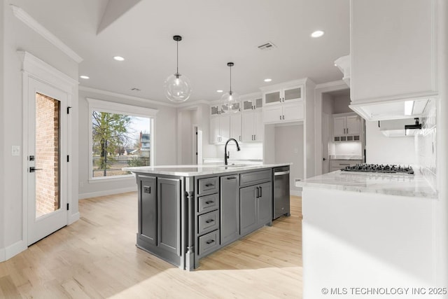 kitchen featuring ornamental molding, stainless steel appliances, white cabinets, hanging light fixtures, and an island with sink