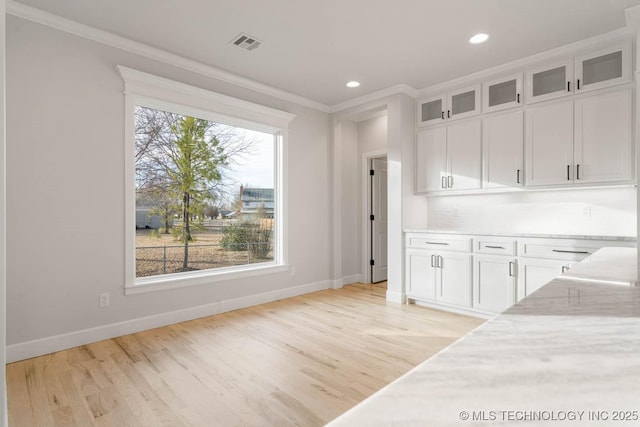 kitchen with white cabinetry, light hardwood / wood-style flooring, a healthy amount of sunlight, and ornamental molding