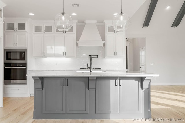 kitchen featuring built in microwave, stainless steel oven, white cabinets, and a center island with sink