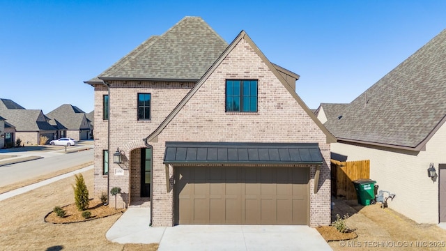 french country inspired facade with concrete driveway, metal roof, roof with shingles, a standing seam roof, and brick siding