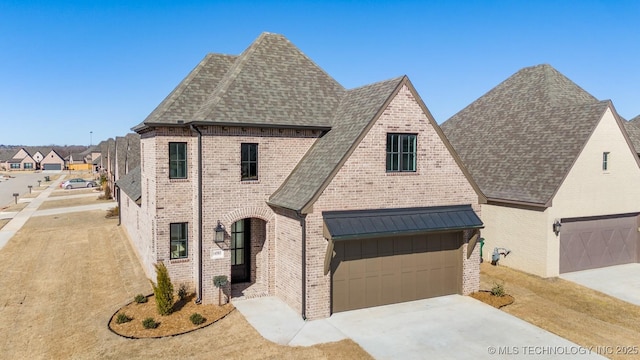 french provincial home with a shingled roof, concrete driveway, brick siding, and a garage