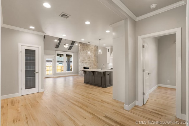 interior space featuring visible vents, light wood-style floors, open floor plan, light countertops, and crown molding