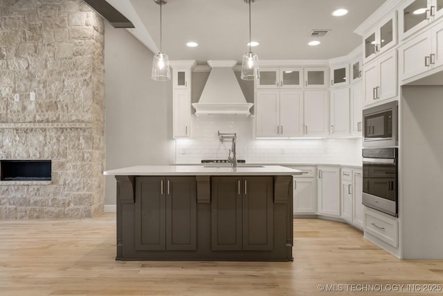 kitchen featuring custom exhaust hood, light countertops, visible vents, built in microwave, and oven