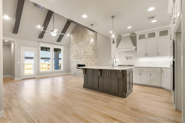 kitchen featuring a fireplace, open floor plan, light countertops, a kitchen bar, and custom range hood