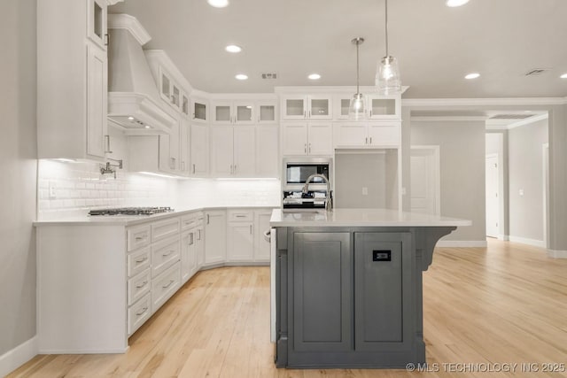 kitchen with premium range hood, appliances with stainless steel finishes, white cabinets, and a sink