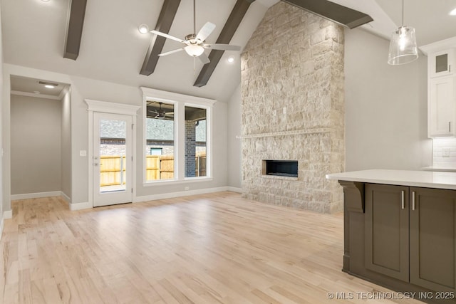 unfurnished living room with a fireplace, a ceiling fan, baseboards, light wood-type flooring, and beamed ceiling